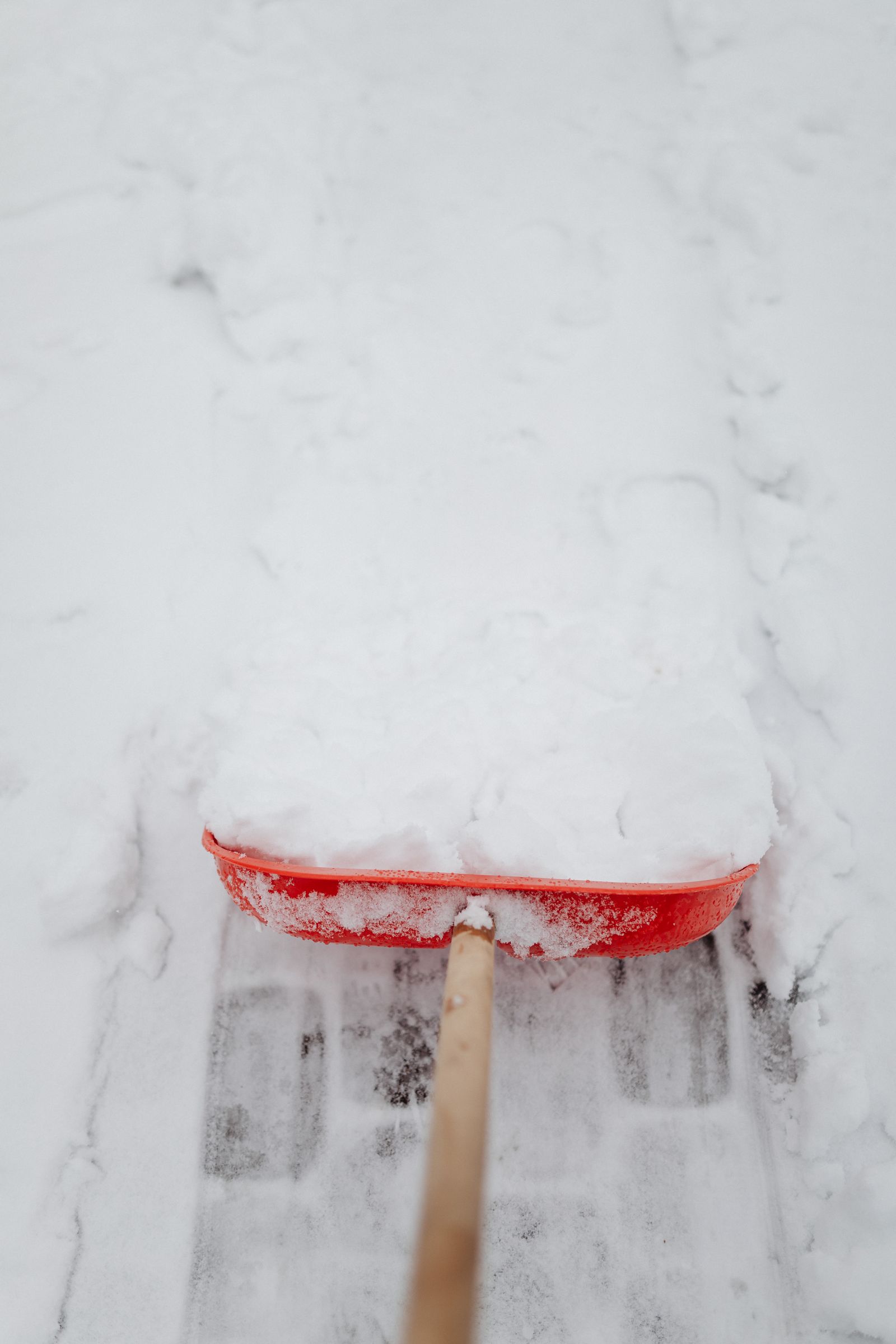 Schneeschaufel im Neuschnee auf einem geräumten Weg