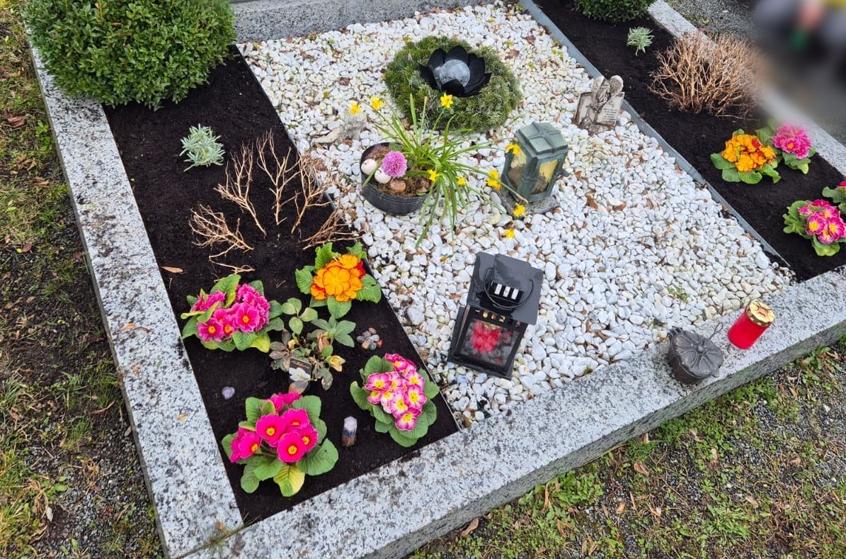Gepflegtes Grab mit bepflanzten Beeten, weißem Kies und Laterne